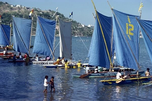 Boats with blue sails line up at the start of a Lakatoi canoe race