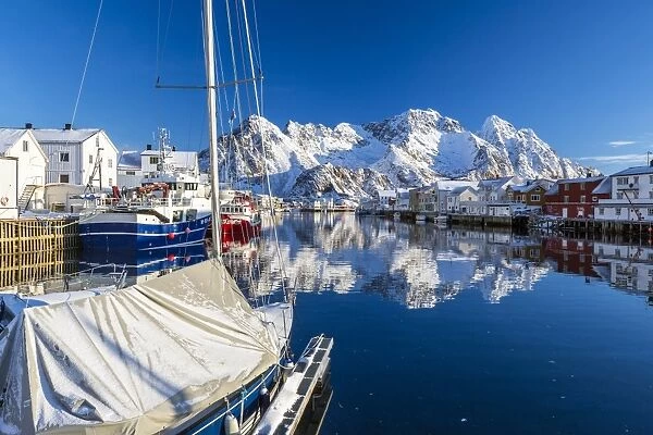 Boats docked in the calm waters of the port of Henningsvaer with the reflection of fishermens houses and Norwegian Alps, Lofoten Islands, Arctic, Norway, Scandinavia, Europe