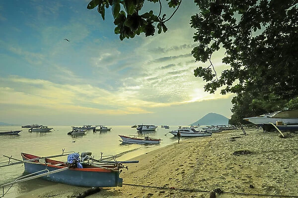 Boats off the town beach at sunset with Manadotua Island beyond on this holiday dive island, Bunaken, North Sulawesi, Indonesia, Southeast Asia, Asia