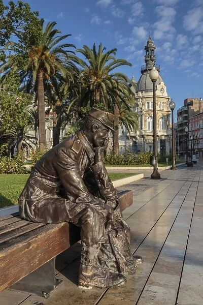 Bronze statue of a sailor on a wooden bench with palm trees, Town Hall backdrop, Cartagena
