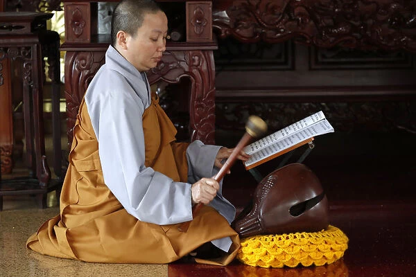 Buddhist ceremony at temple, monk playing on a wooden fish (percussion instrument)