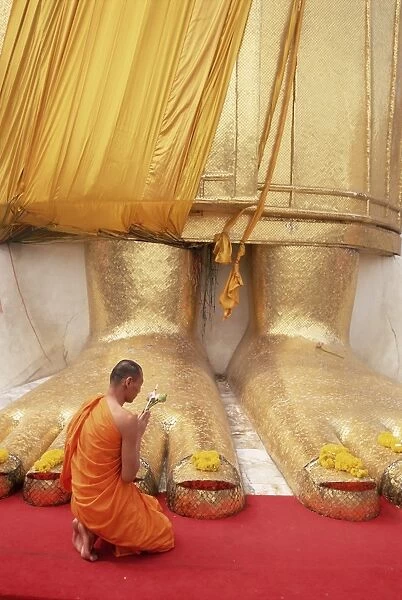 Buddhist monk kneeling in prayer at the feet of a statue