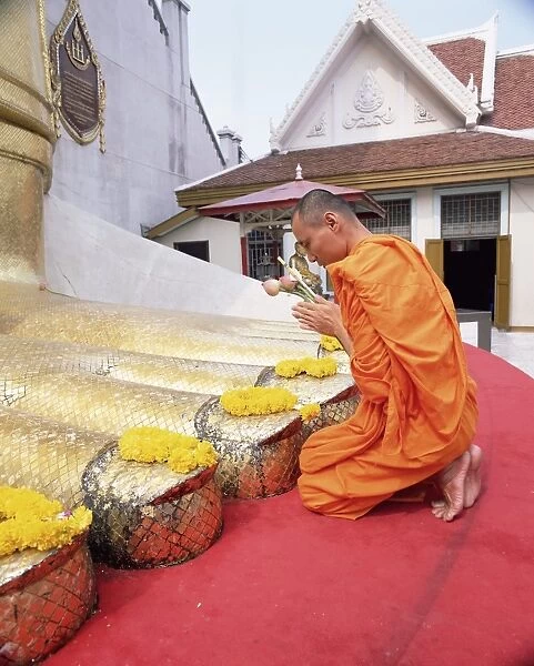 Buddhist monk kneeling and praying at the feet of a standing Buddha