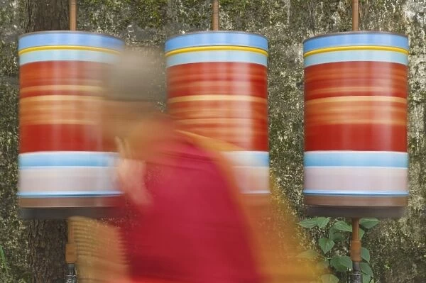 Buddhist monk passing prayer wheels