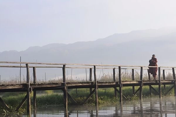 Buddhist monk, walking in the early morning on a wooden walkway, Inle Lake