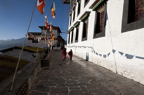 Buddhist monks in red robes walking in the early morning sunshine on the walls of Tawang Buddhist monastery, Arunachal Pradesh, India, Asia