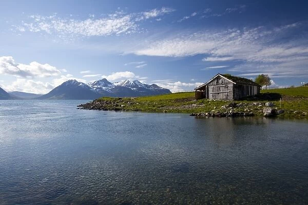 Cabin with traditional grass roof overlooking a fjord and snowy mountains in Lyngen Peninsula