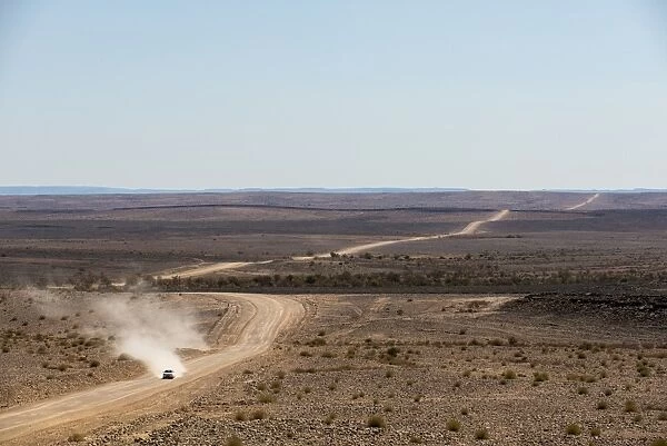 A car leaves a cloud of dust as it apporachs along the long dusty road from the Fish River Canyon