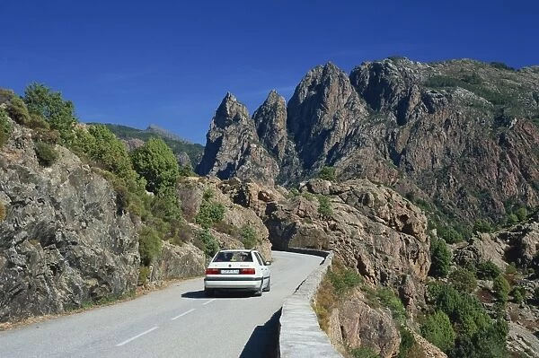 Car on mountain road above the Spelunca Gorge, with Capo Ferolata behind