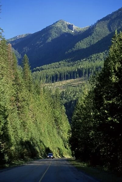 Car on Route 31A dwarfed by steep tree-covered slopes, near Kaslo, British Columbia (B