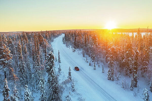 Car travels the icy and empty road crossing the boreal snowy forest at sunrise, Swedish Lapland, Sweden, Scandinavia, Europe