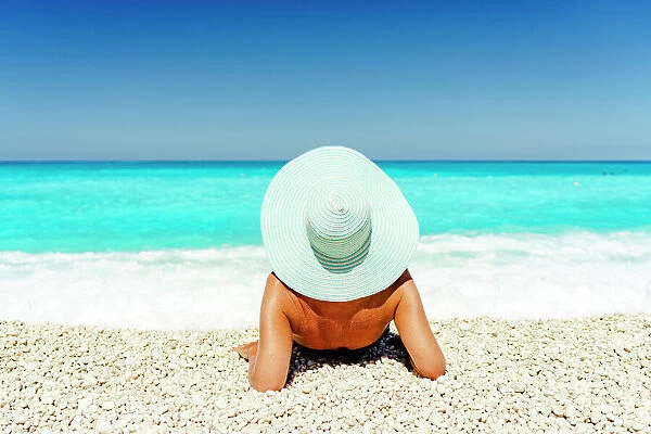 Carefree woman with straw hat sunbathing lying on a idyllic beach, Kefalonia, Ionian Islands, Greek Islands, Greece, Europe