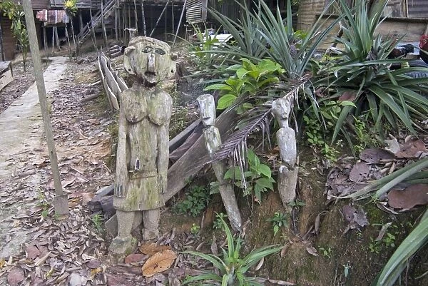 Carved spirits of men and a woman standing at the entrance to Iban tribal longhouse at Ngemah beach on the Lemanak River, Sarawak, Malaysian Borneo, Malaysia, Southeast