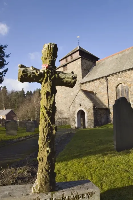 Framed Print : Carved stone cross headstone in front of the 14th century St Framed Print : Carved stone cross headstone in front of the 14th century St