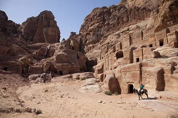 Child riding a donkey in front of cave dwellings in Petra, UNESCO World Heritage Site, Jordan, Middle East