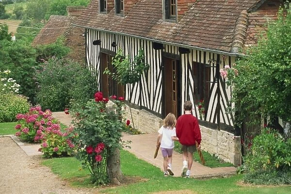 Children carrying baguettes in front of a typical half timbered cottage near St