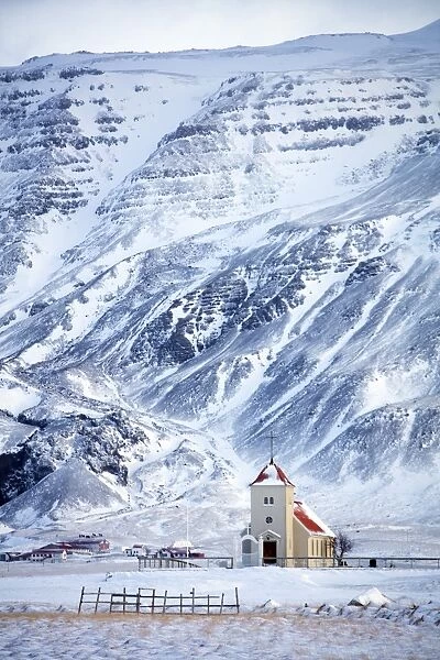 Church and isolated farm against snow covered mountains, winter afternoon on the