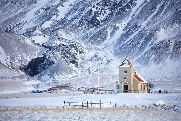 Church and isolated farm against snow covered mountains, winter afternoon on the