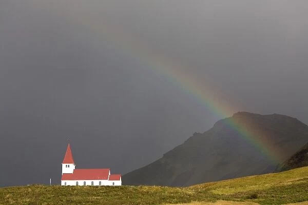 Church and rainbow against stormy sky and mountains, Vik Y Myrdal, South Iceland