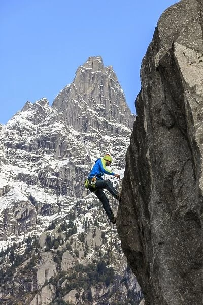 Climber on steep rock face in the background blue sky and peaks of the Alps, Masino Valley