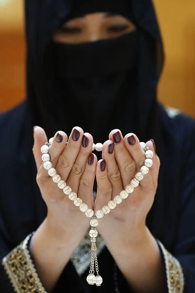 Close up of a Muslim womans hands in abaya while holding rosary and praying