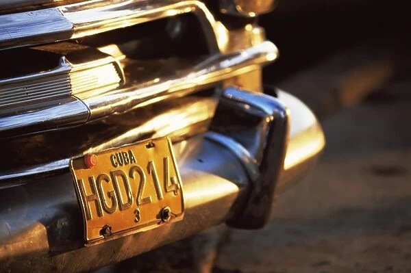 Close-up of chrome bumper and yellow car number plate in morning light