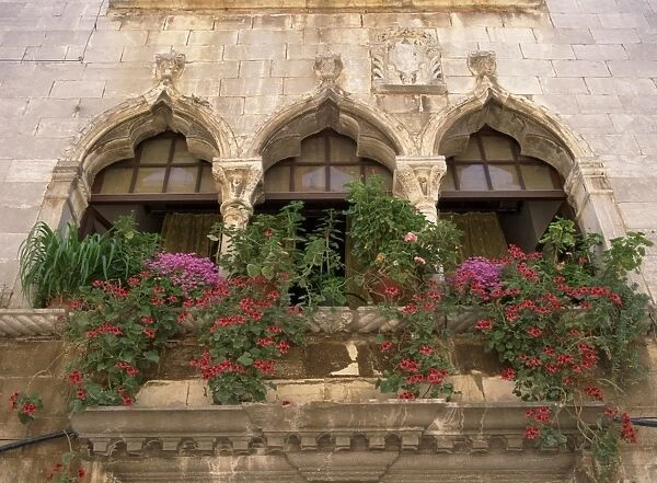 Close-up of ornate window arches with pots of oxalis and geraniums on the balcony at Porec