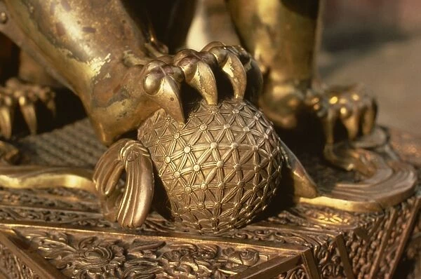 Close-up of the paw of a gilt bronze lion holding a fire ball, symbol of force