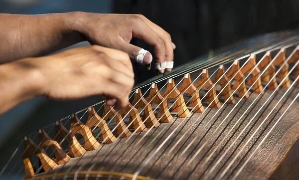 Closeup of two hands playing the guzheng, a traditional Chinese string instrument