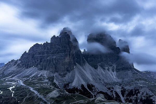 Clouds at dusk in the foggy sky over Tre Cime di Lavaredo mountain peaks, Dolomites, South Tyrol, Italy, Europe