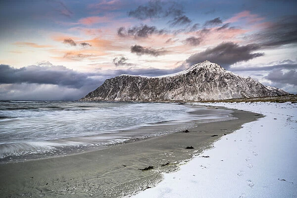 Clouds at sunset over mountain peak covered with snow and icy Skagsanden beach, Flakstad