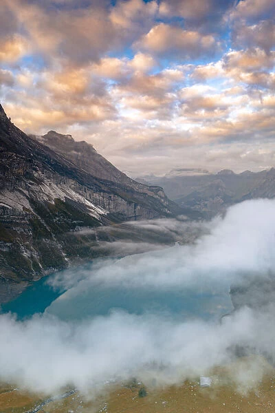 Clouds at sunset over the pristine lake Oeschinensee in the mist, Bernese Oberland
