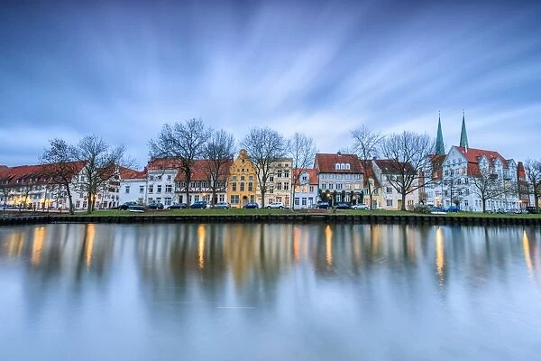 Clouds on the typical houses and towers of cathedral reflected in River Trave at dusk