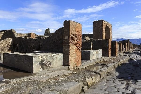 Cobbled street with thermopolium counters and arch, Roman ruins of Pompeii, UNESCO