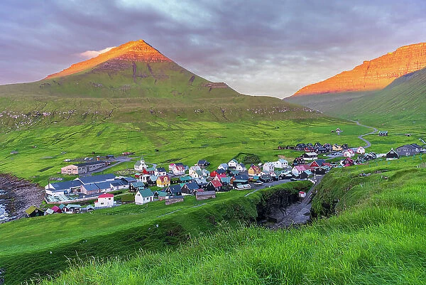 Colorful houses of the village of Gjogv with the mounatins lit by the early sun, sunrise view, Eysturoy island, Faroe islands, Denmark, Europe