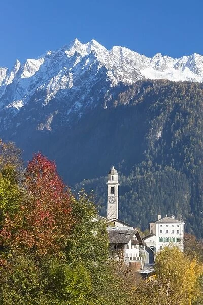 The colorful trees frame the alpine church and the snowy peaks, Soglio, Bregaglia Valley