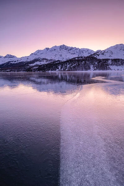 Colors of sunrise is reflected on the icy surface of Lake Sils, Engadine Valley