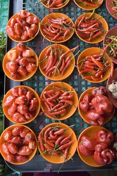 Colourful red chillies and capsicums on orange plates on a market stall in Kuching
