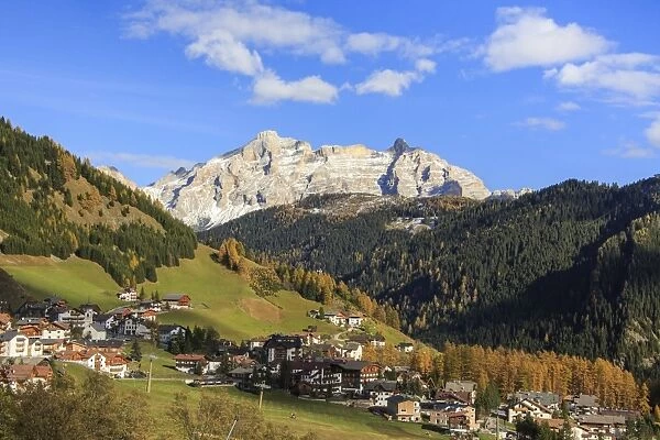 Colourful woods frame the village and the high peaks in autumn, Gardena Pass, South Tyrol