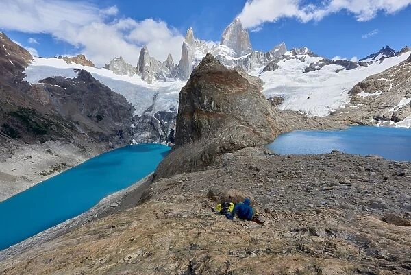 A couple in mountain gear rests on rocks with view to Lago de los Tres and Mount Fitz Roy