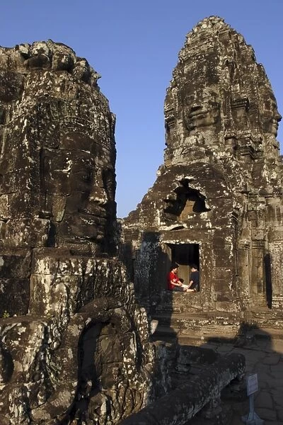 A couple rest beneath the giant faces of the Bayon temple, Angkor, UNESCO World Heritage Site