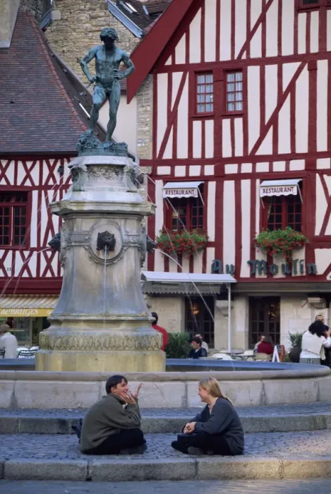 Framed Print : A couple sit in front of a fountain in the Place Francois Rude, with half timbered houses behind Framed Print : A couple sit in front of a fountain in the Place Francois Rude, with half timbered houses behind