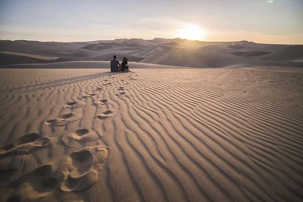 Couple watching the sunset over sand dunes in the desert at Huacachina, Ica Region