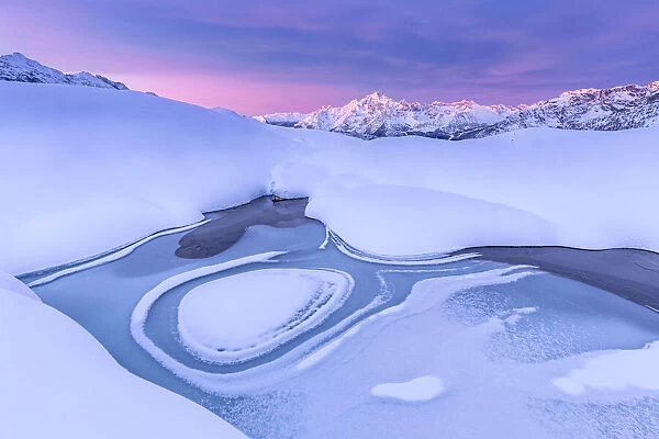 Crazy shape in a frozen alpine lake at sunrise with view of Mount Disgrazia, Valmalenco