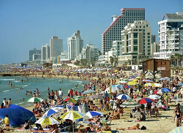 Crowds of tourists on the beach with tall seafront buildings, at Tel Aviv