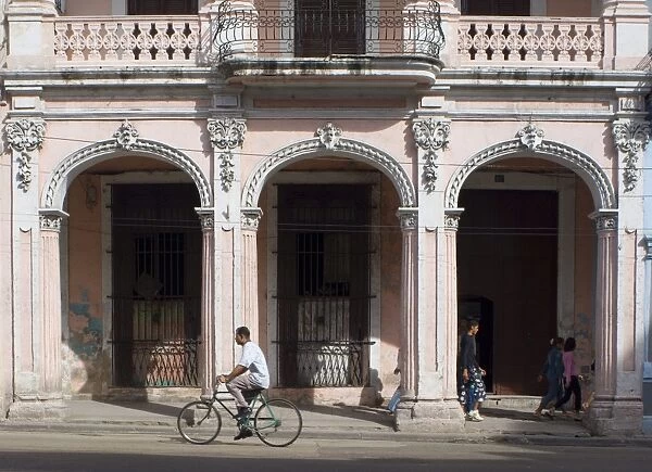 A cyclist passing an ornate old building on Avenida Reina in central Havana
