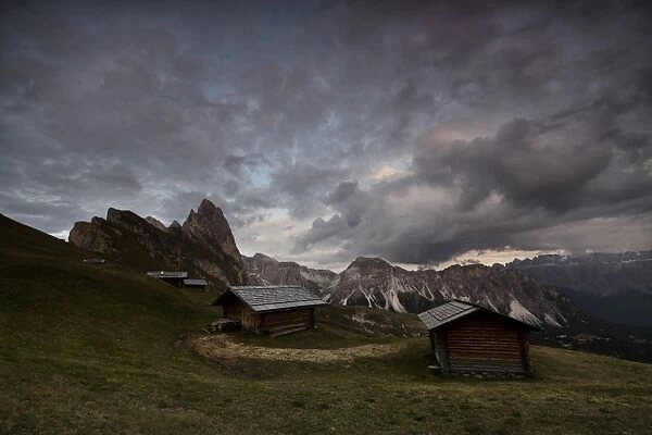 Dark clouds on green meadows and huts of the Odle mountain range seen from Seceda
