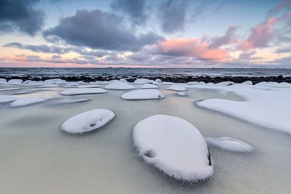 Dawn on the cold sea surrounded by snowy rocks shaped by wind and ice at Eggum, Vestvagoy