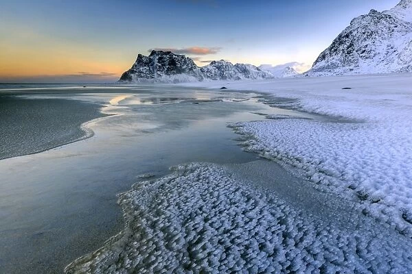 Dawn illuminates the beach covered with frozen snow in the cold sea of Uttakleiv