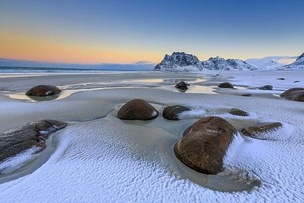 Dawn illuminates the rocks shaped by wind surrounded by fresh snow, Uttakleiv, Lofoten Islands